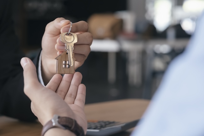 La mano di un agente immobiliare consegna le chiavi dell'acquisto di una casa nella mano di un altro uomo, felice di aver analizzato i Vantaggi di usare un'agenzia immobiliare